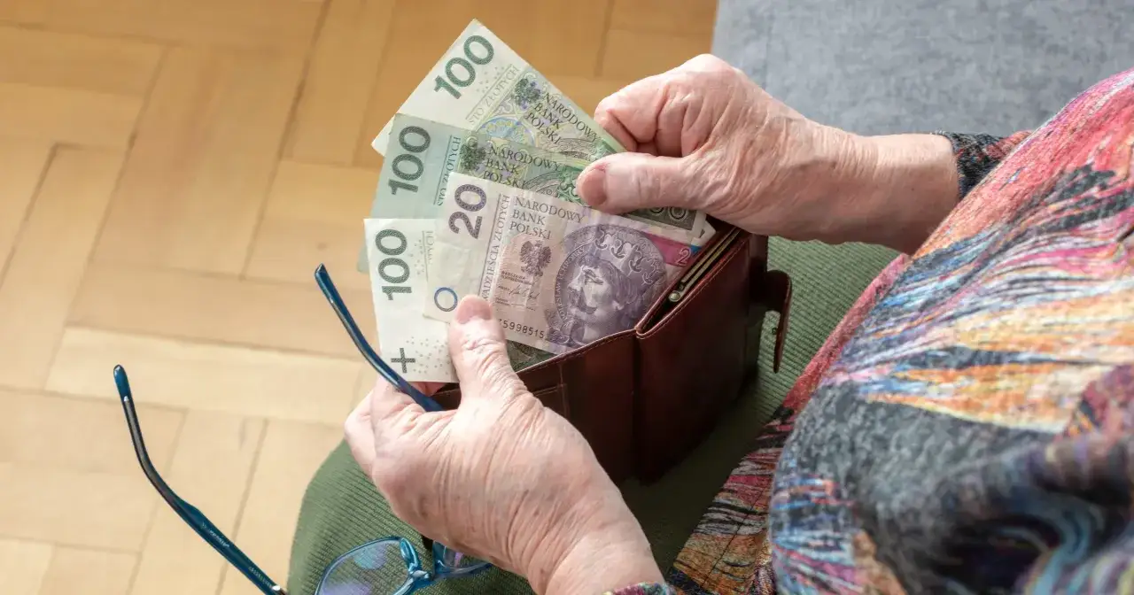 Dłoń starszej osoby wkłada pieniądze do portfela. To symbol troski o przyszłość i waloryzację emerytur i rent.