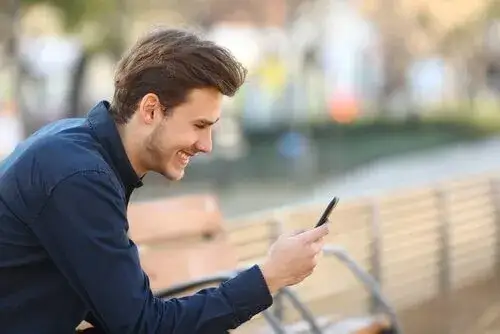 mężczyzna piszący na telefonie z uśmiechem, pewny siebie, randkowanie online