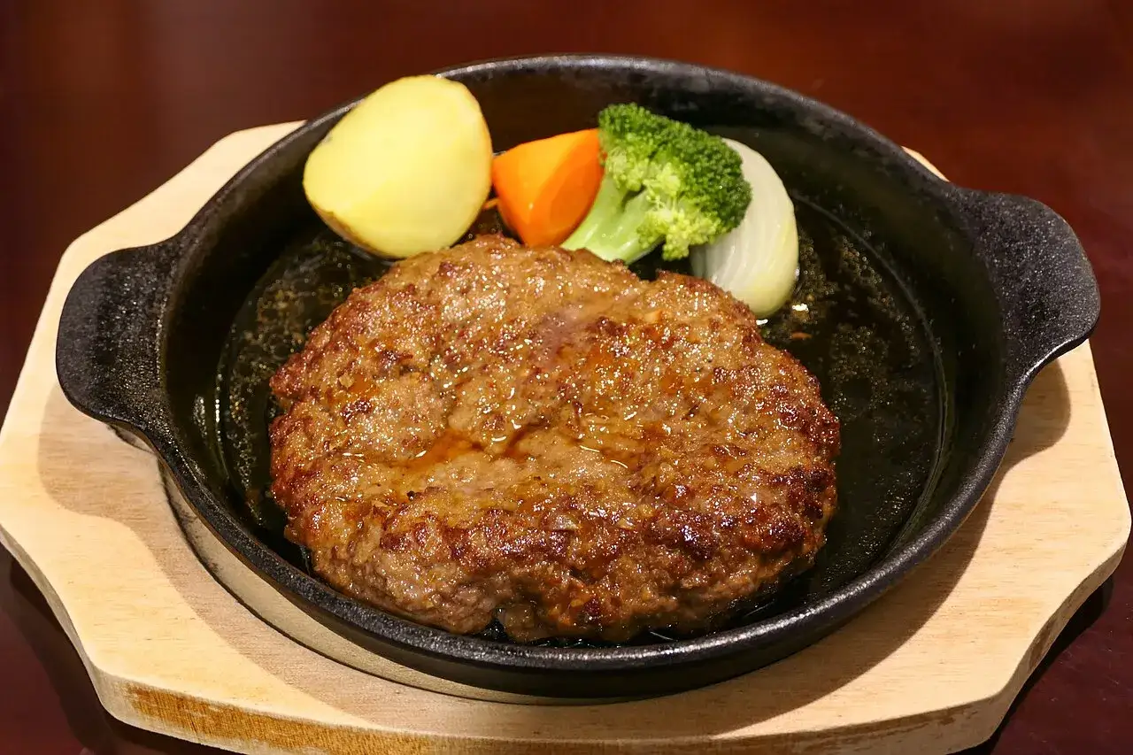Un steak haché juteux, d'où vient le burger, servi avec des pommes de terre, des carottes, du brocoli et de l'oignon dans une poêle chaude.