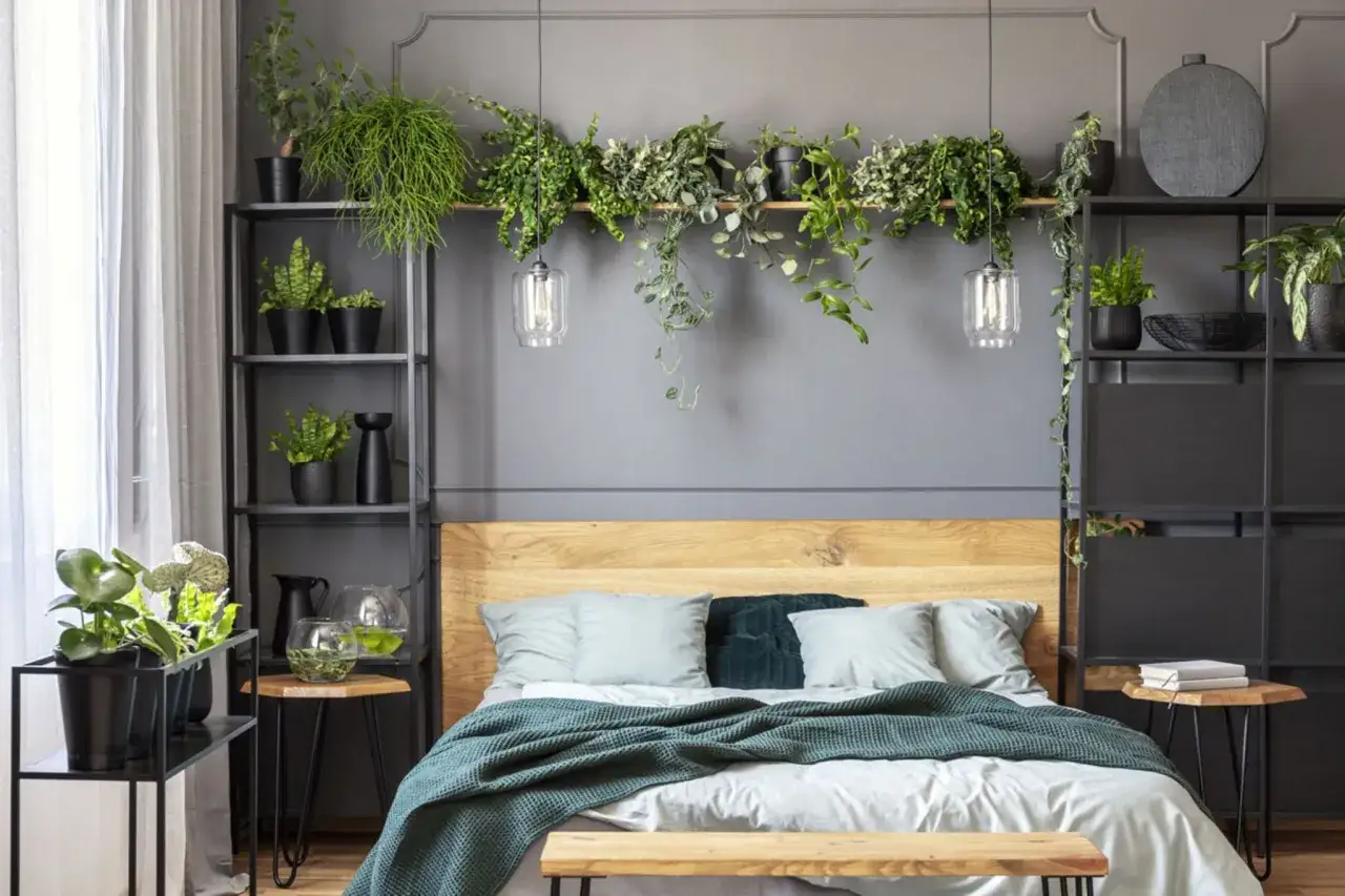 Ein gem&uuml;tliches Schlafzimmer mit vielen gr&uuml;nen Pflanzen, die &uuml;ber dem Bett h&auml;ngen und auf Regalen stehen. Die Pflanzen im Schlafzimmer schaffen eine entspannte Atmosph&auml;re.