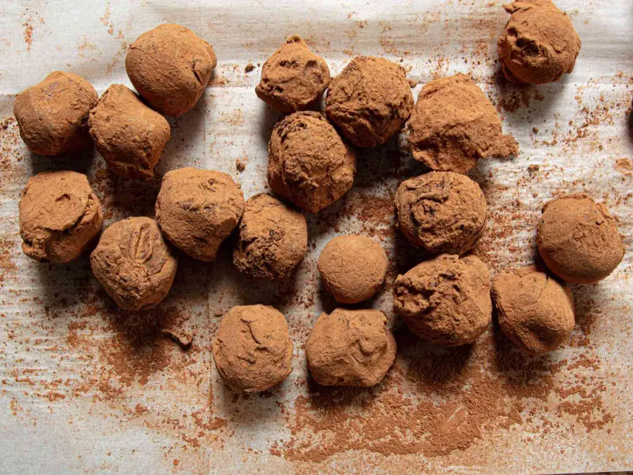 Un surtido de trufas de chocolate cubiertas de cacao en polvo, espolvoreadas sobre papel de horno.