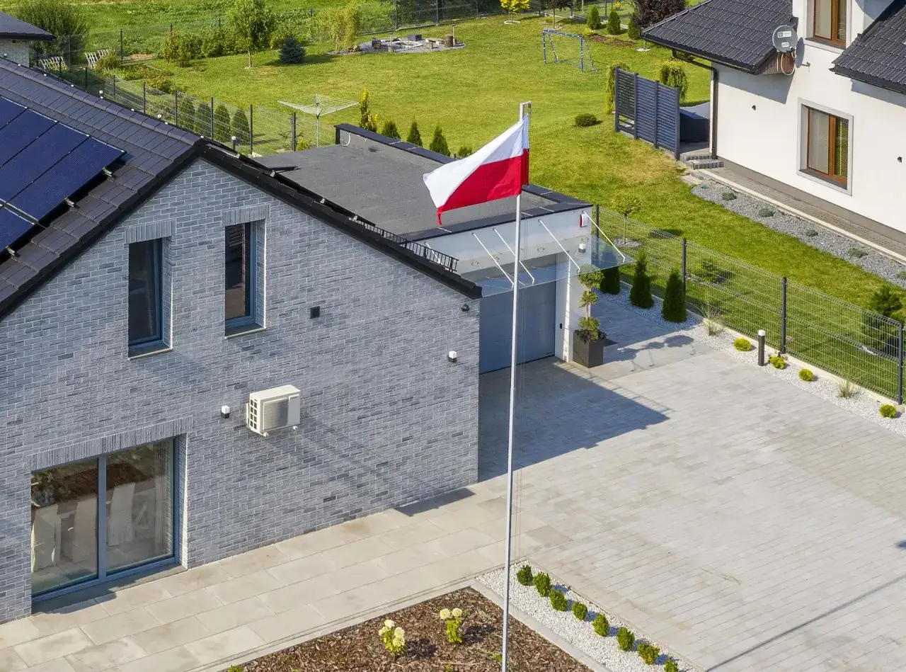 Nowoczesny dom z panelem słonecznym i polską flagą na maszcie. Czy flaga może wisieć cały rok? Tak, jeśli jest symbolem dumy i przynależności.
