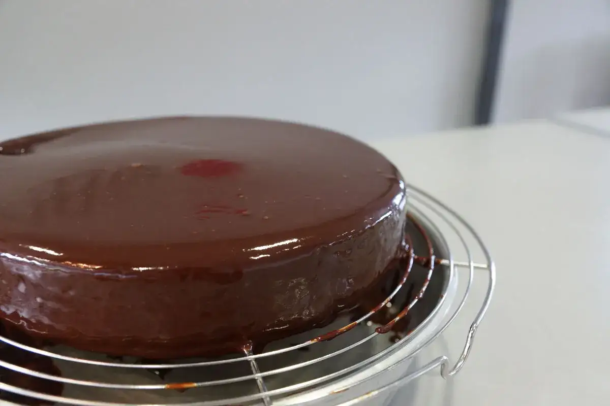 Gâteau rond et brillant, recouvert d'un glaçage chocolat beurre onctueux. Quelques gouttes de glaçage coulent sur la grille.