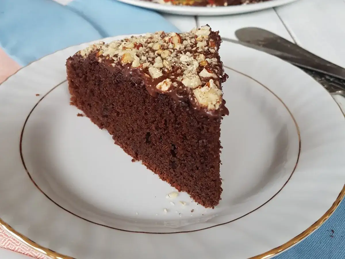 Una fetta di torta barbabietola e cioccolato, umida e ricca, guarnita con glassa al cioccolato e noci tritate.