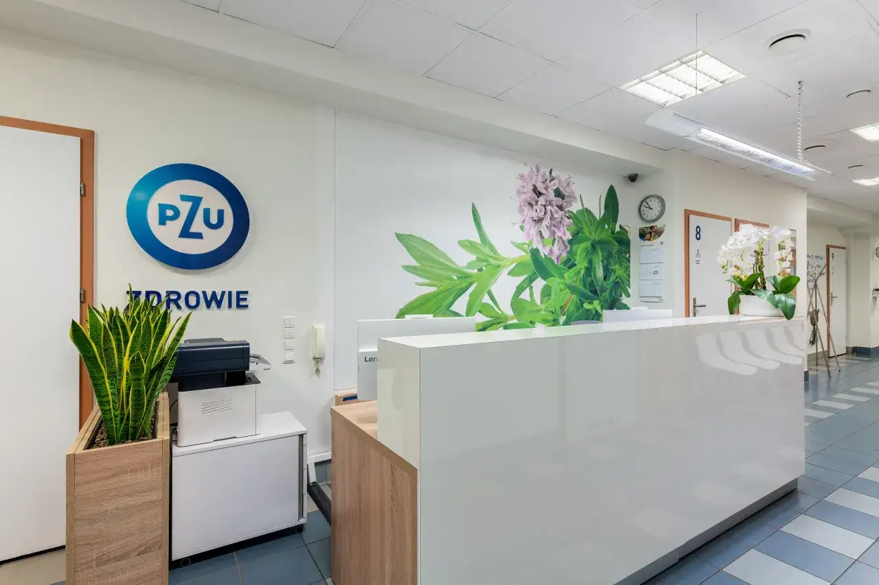 Recepcja placówki medycznej PZU Zdrowie z roślinami i grafiką kwiatów na ścianie.