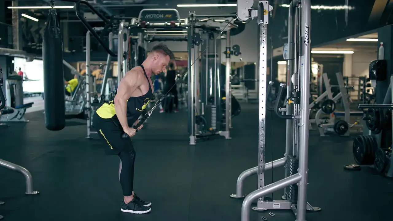 Mężczyzna wykonuje ćwiczenia na narty, trenując triceps przy użyciu wyciągu.