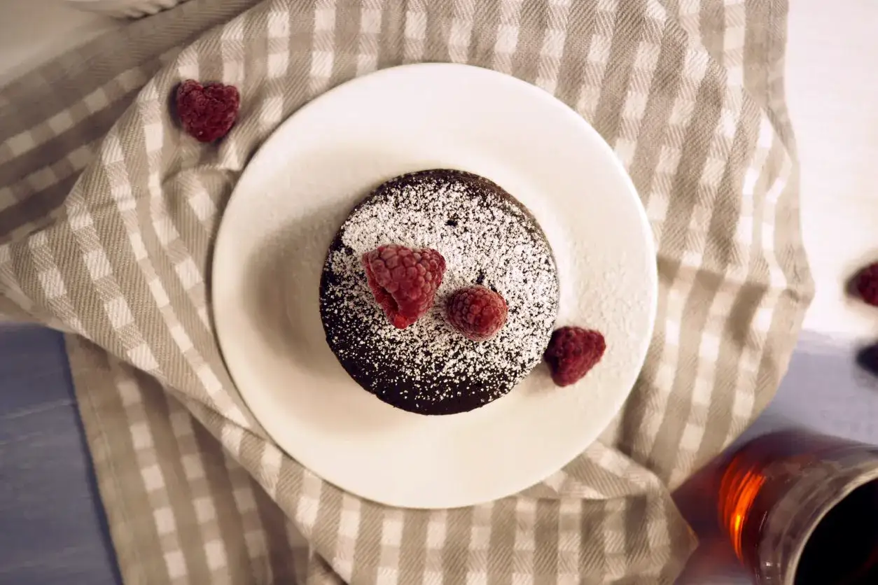 Pyszny, gorący lava cake z mikrofali, posypany cukrem pudrem i ozdobiony malinami. Idealny deser na szybko.