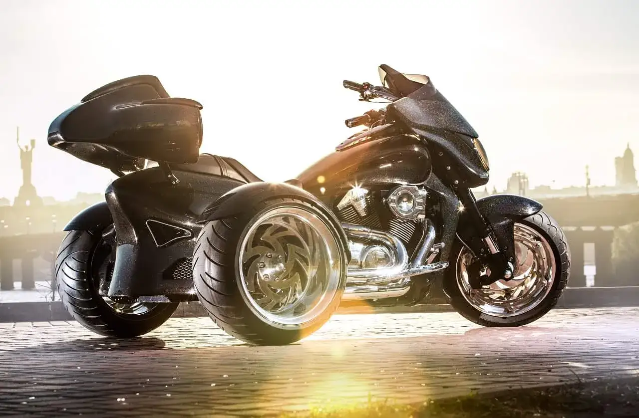 Czarny, lśniący motocykl trójkołowy na kat B. Z dumą prezentuje swoje potężne koła i chromowane detale na tle miejskiego krajobrazu.