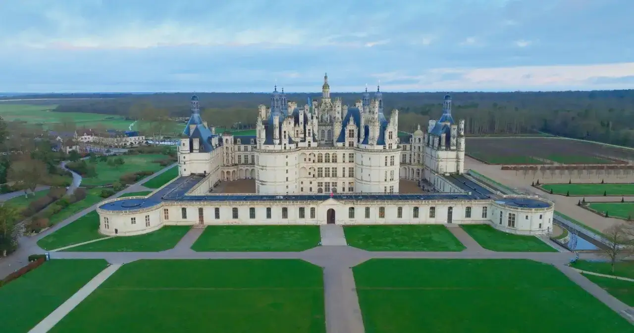 Imponujący zamek Chambord, jeden z największych zamków w Europie, otoczony zielonymi ogrodami i lasem.