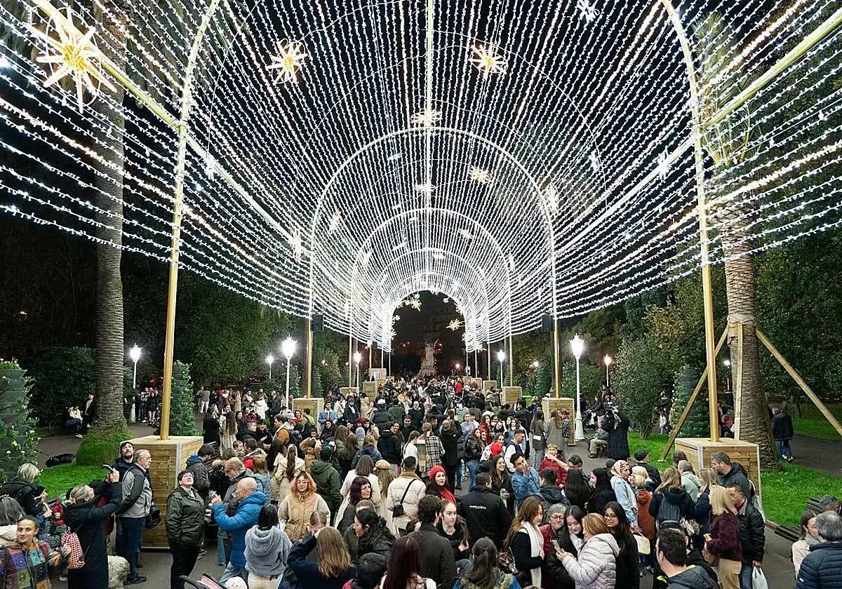 Gente pasea bajo un túnel de luces navideñas en el parque Doña Casilda, creando un ambiente mágico y festivo.