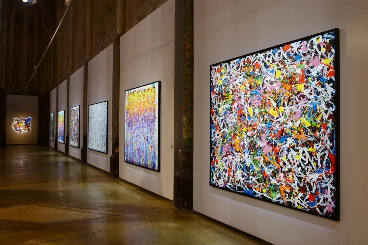 Exposition d'art avec des toiles color&eacute;es et abstraites, dont une grande pi&egrave;ce de JonOne, cr&eacute;ant une explosion visuelle.
