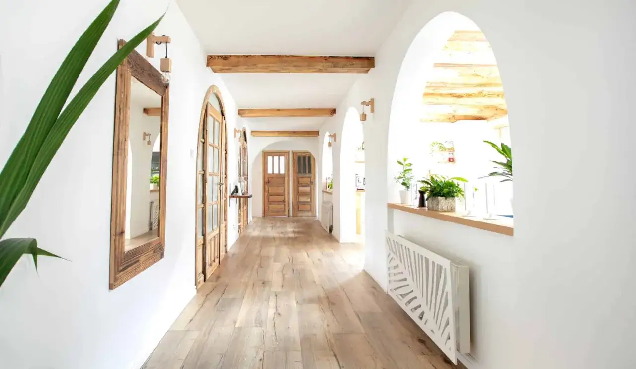 A rustic hallway with wooden doors and beams. A tall mirror with a wooden frame reflects the space, its mirror size adding depth.