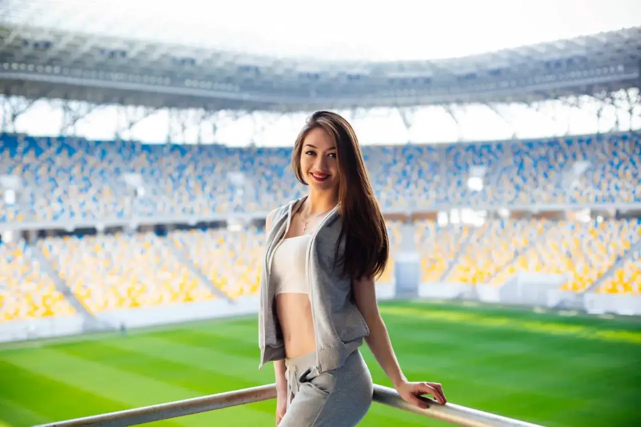 Uśmiechnięta dziewczyna w sportowym stroju na tle stadionu. Idealny pomysł, jak się ubrać na mecz, by czuć się komfortowo i stylowo.
