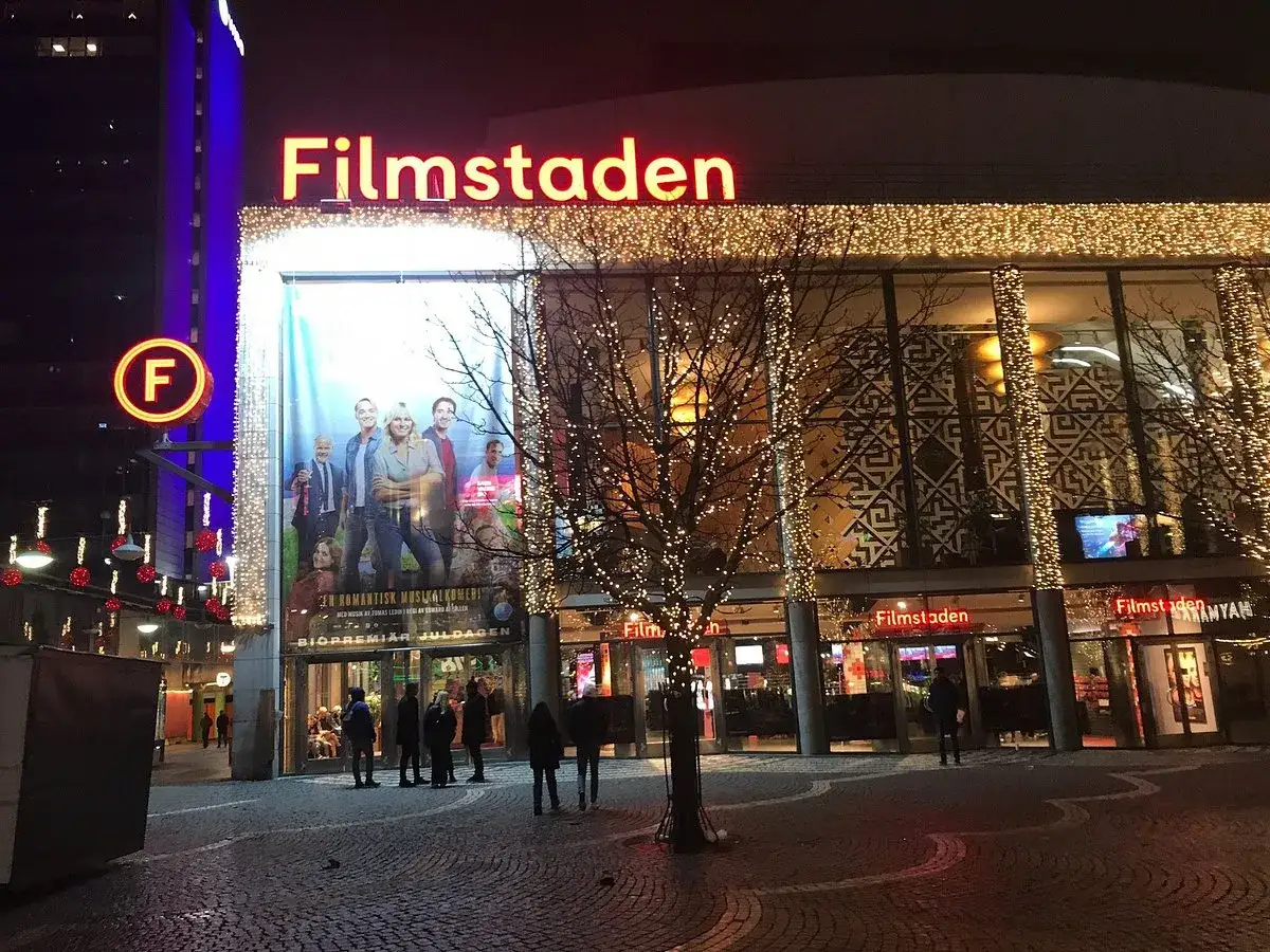Filmstaden vid Sergels torg lyser upp en mörk kväll. En stor filmaffisch och julbelysning skapar en festlig stämning.