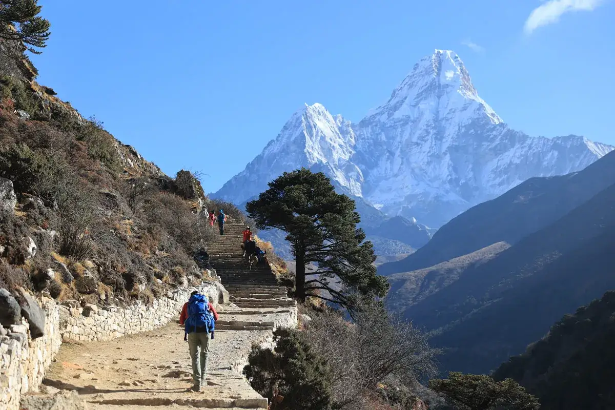 Turyści wspinają się po kamiennych schodach w kierunku bazy pod Mount Everest. W tle majestatyczne, ośnieżone szczyty.
