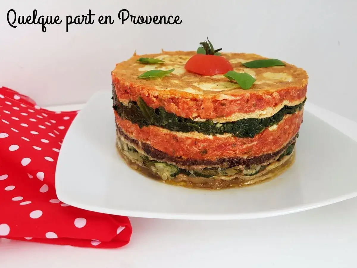 Le crespeou, une tour de légumes et de viande, ornée d'une tomate cerise et de basilic, sur une assiette blanche.