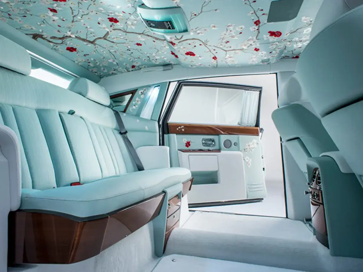Wnętrze Rolls-Royce z kwiecistym motywem na suficie i drzwiach. Luksusowe siedzenia i detale sugerują wysoką rolls royce cena.