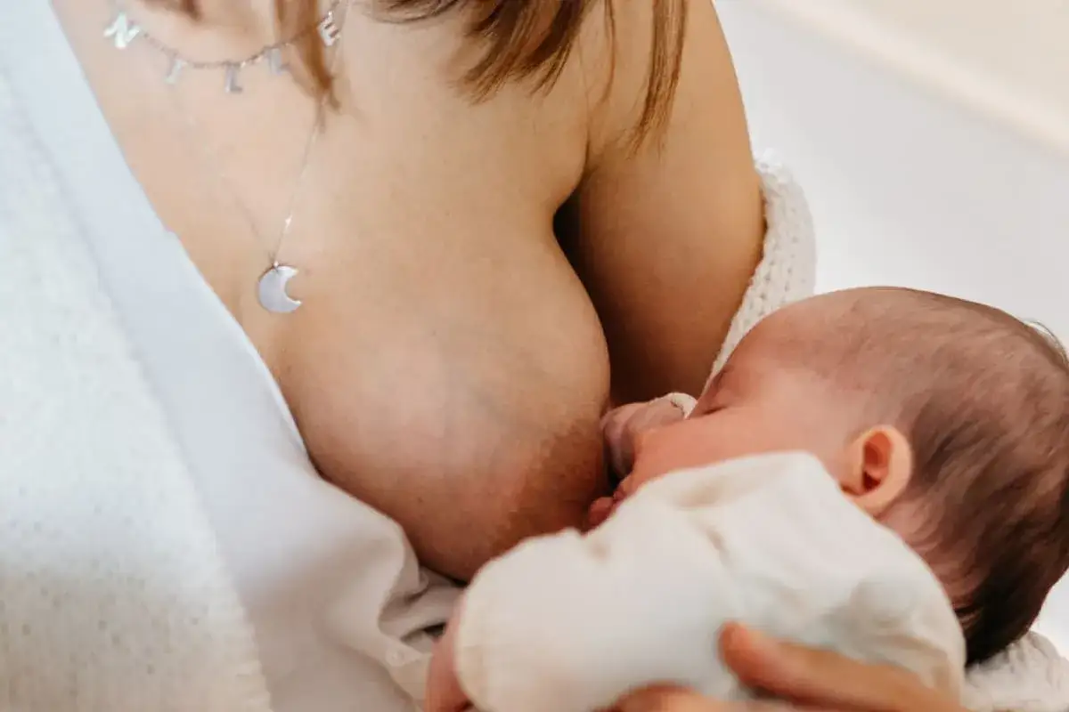 Un neonato si nutre al seno, un momento intimo che celebra la produzione latte materno. La mamma indossa una collana con una luna.