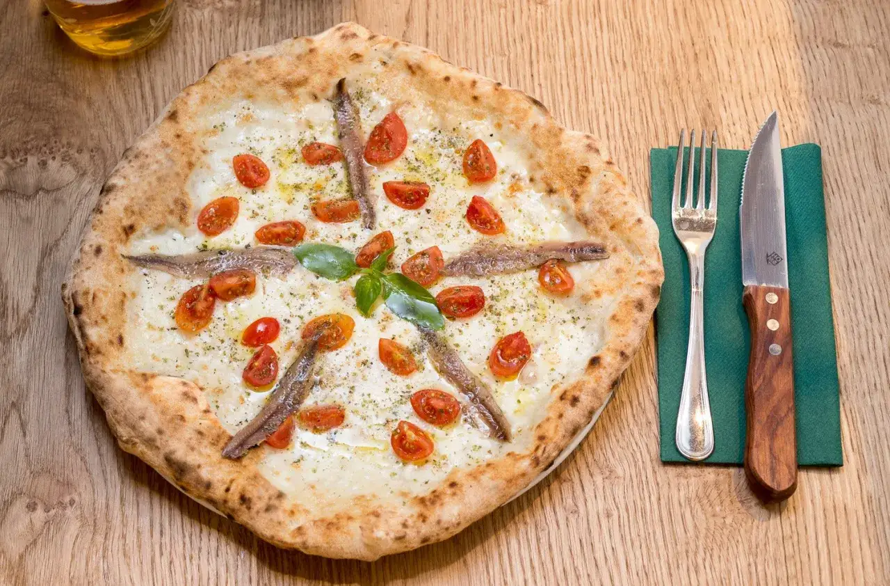 Pizza con acciughe e pomodorini, pronta per essere gustata con una birra rinfrescante.