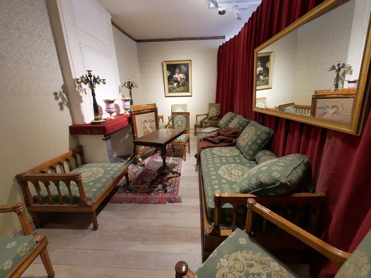 Salon du chateau de Saché, avec canapés fleuris, tapis persan et grand miroir reflétant une pièce élégante.