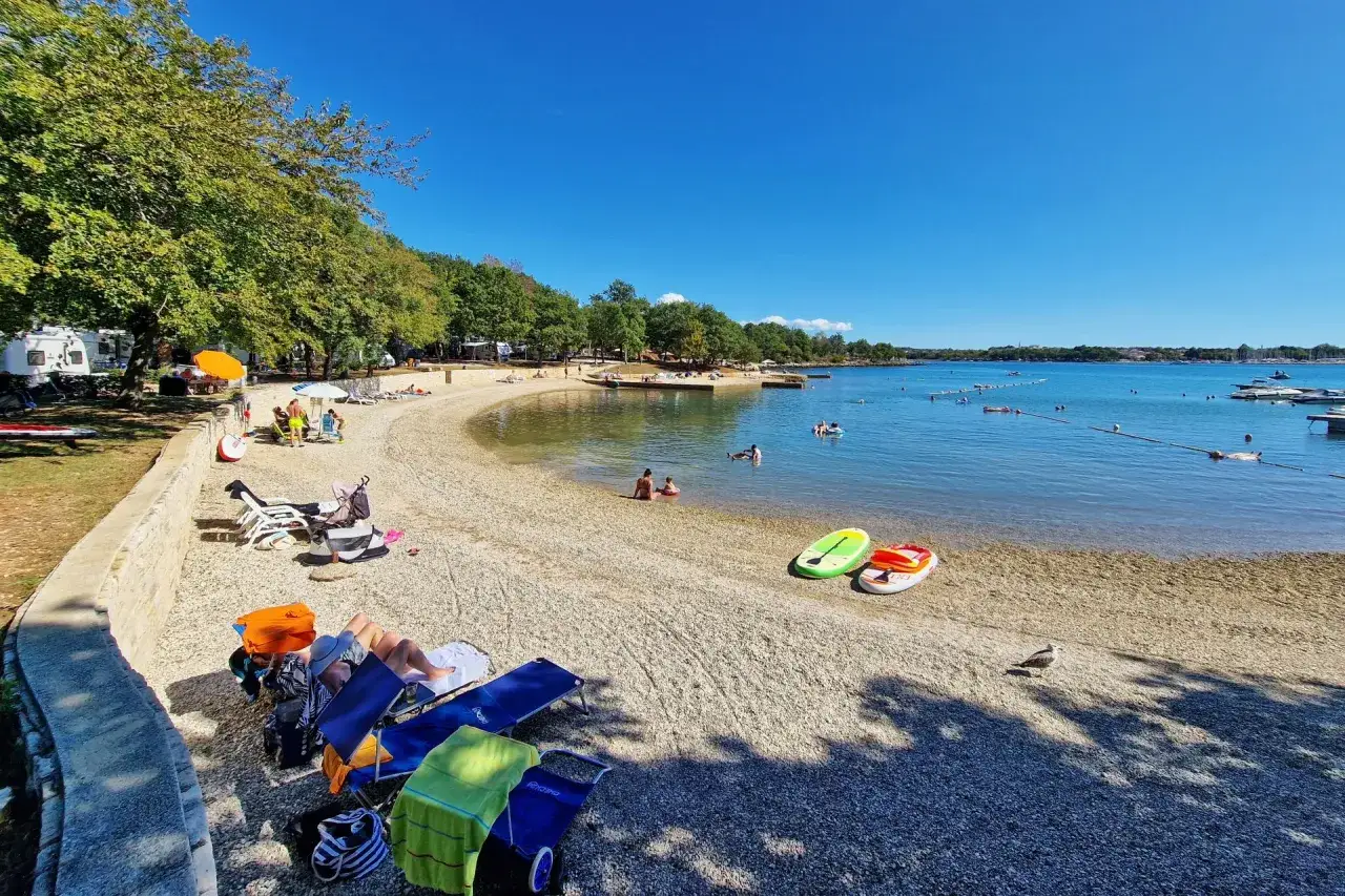 Słoneczny dzień na plaży w **camping Bijela Uvala**. Leżaki, parasole i spokojne morze zachęcają do relaksu.