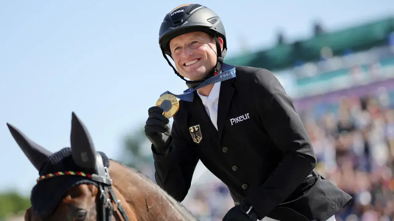 Michael Jung strahlt mit seiner Goldmedaille auf dem Pferd.