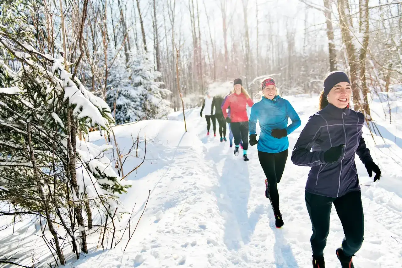 Frauen laufen im Winter, gekleidet in warme Sportkleidung, durch einen verschneiten Wald.