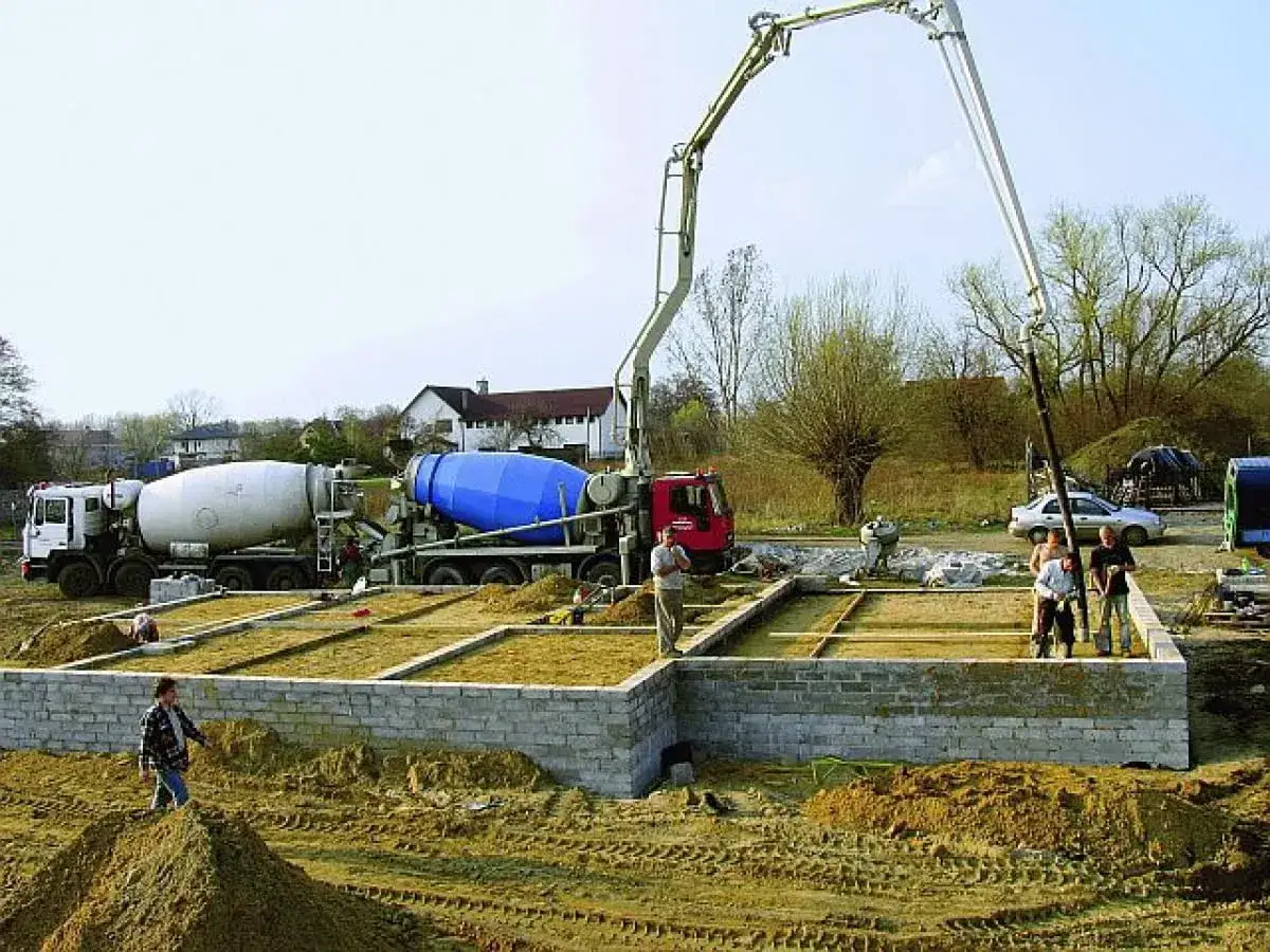 Betonowanie fundamentów pod dom. Dwie betoniarki i pompa do betonu pracują na budowie. To kluczowy etap, który wpływa na to, ile kosztuje budowa fundamentów pod dom.