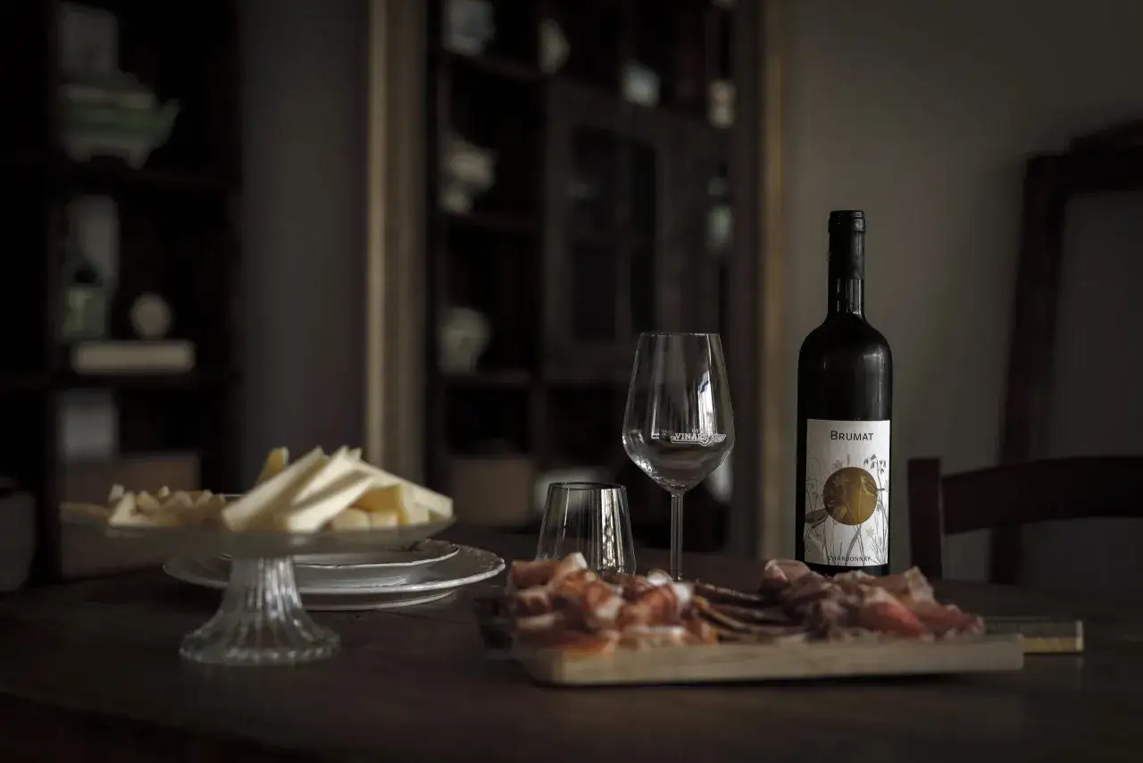 Un calice, salumi e formaggi su un tavolo di legno, con una bottiglia di vino