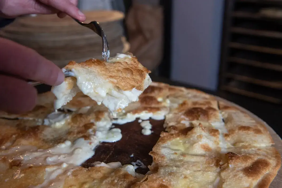 Una fetta di focaccia di Recco, con il suo formaggio filante, viene sollevata con una forchetta.