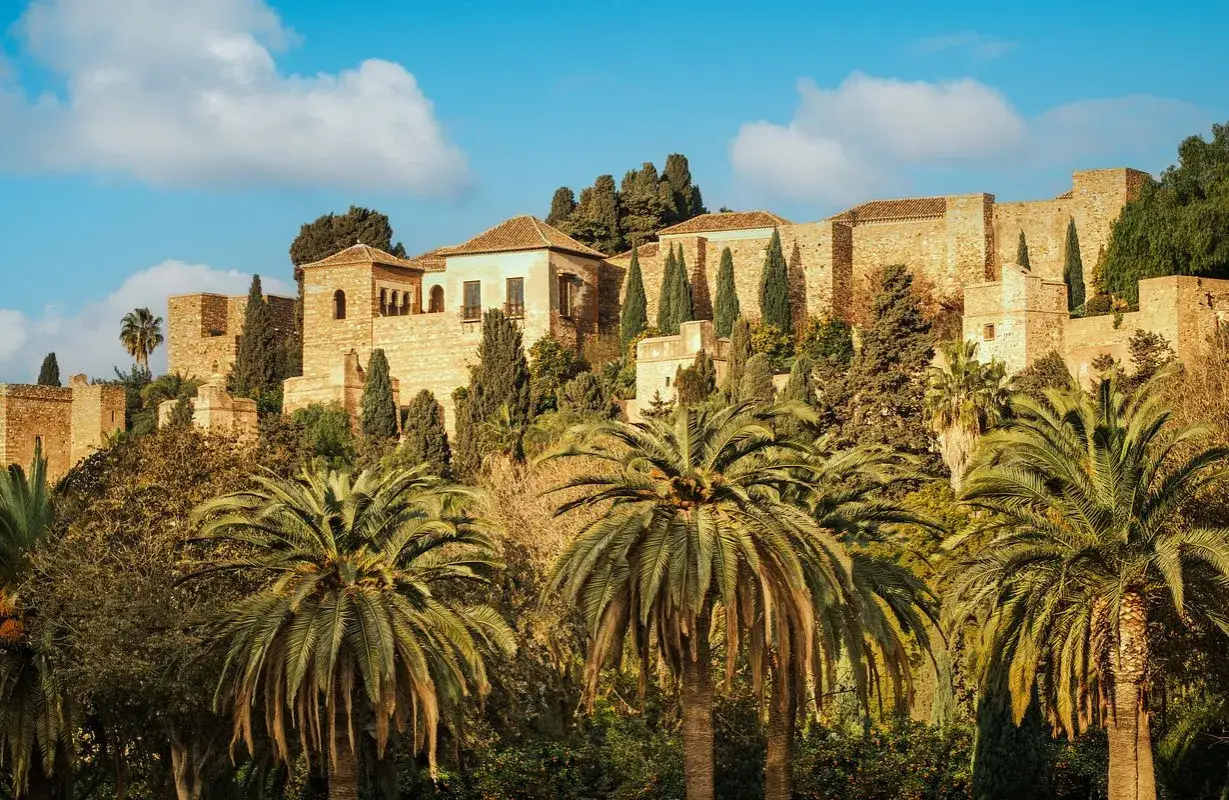 Vue d'une forteresse historique sur une colline, entourée de palmiers et de cyprès. Une belle idée pour savoir que faire à Malaga.