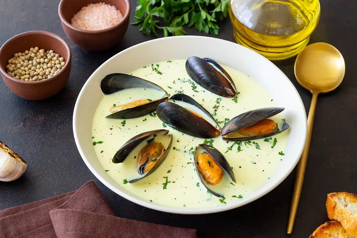 Ein Teller cremiger Muscheln, perfekt zum Genie&szlig;en mit einem Glas Wein. Beilagen wie Knoblauch, Kr&auml;uter und Gew&uuml;rze deuten auf ein k&ouml;stliches Gericht hin.
