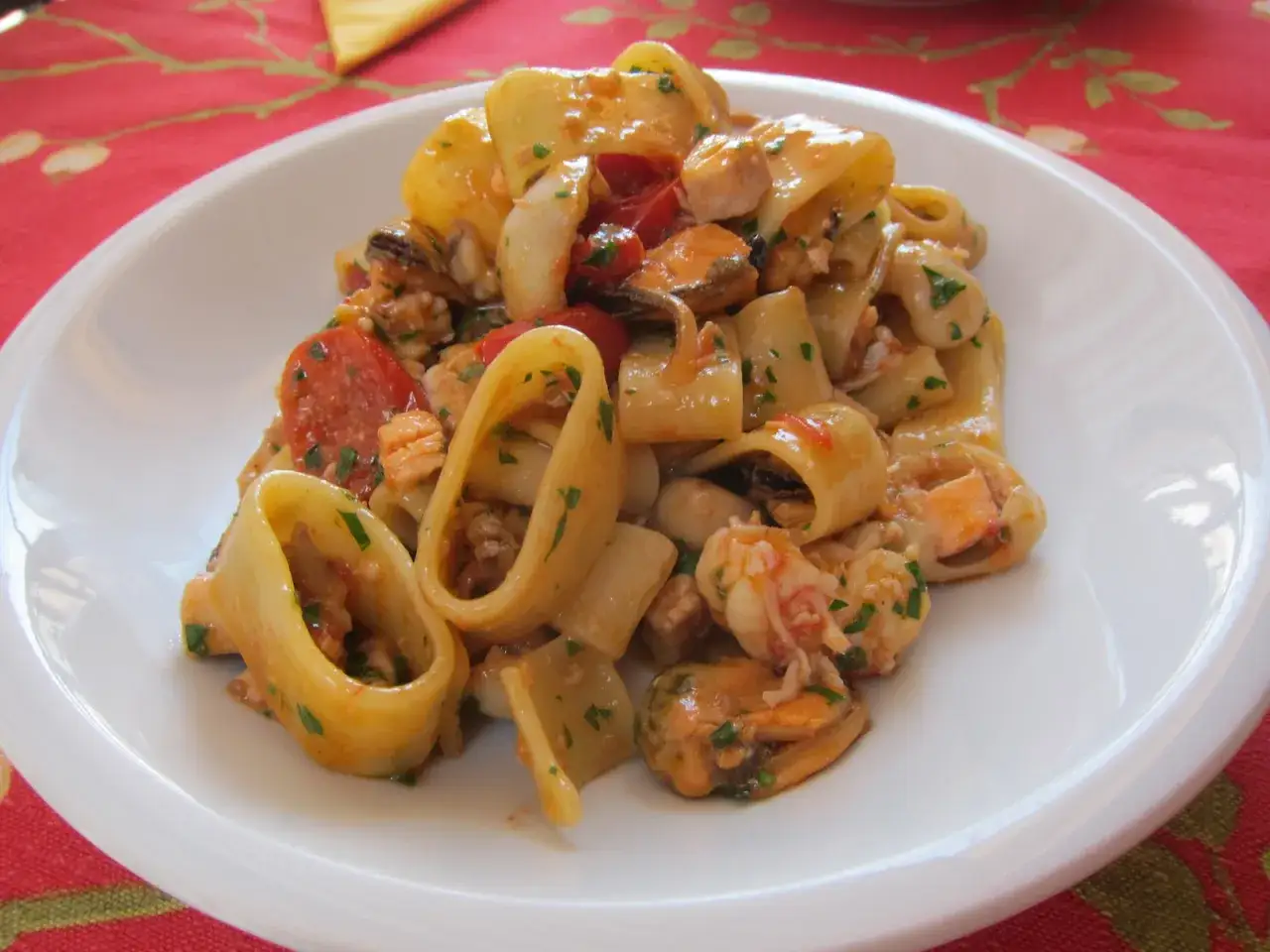 Un piatto invitante di calamarata allo scoglio, con pasta grossa, cozze, gamberi e pomodorini, condita con prezzemolo fresco.