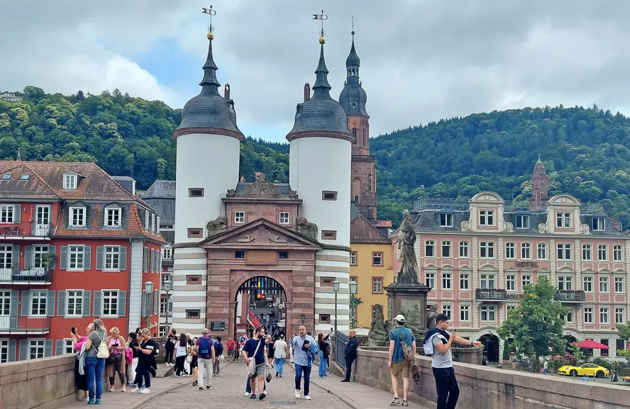 Menschen spazieren &uuml;ber die Alte Br&uuml;cke in Heidelberg, ein perfekter Ort f&uuml;r Fotos mit Blick auf die T&uuml;rme und die Altstadt.