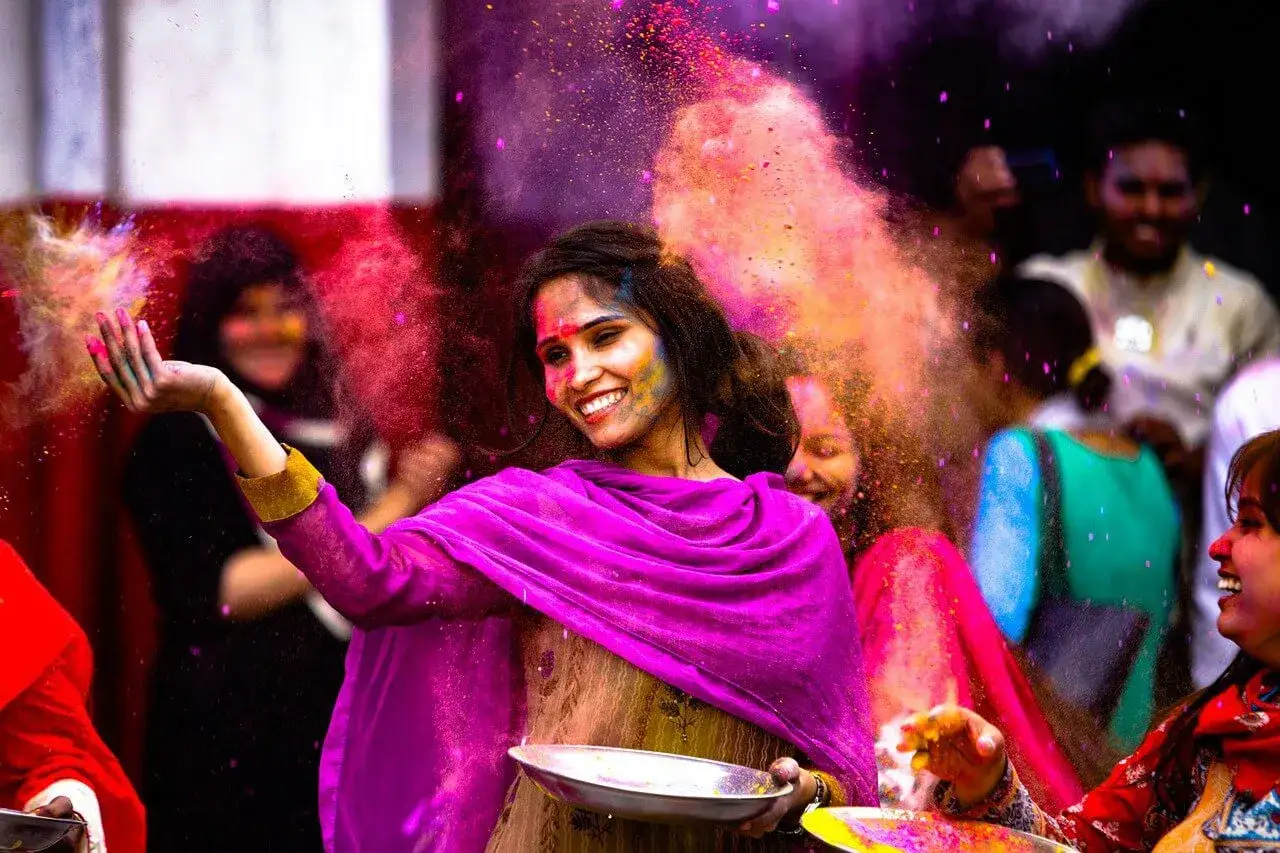 Junge Frau lacht, während sie beim Holi Festival in Indien bunte Pulver in die Luft wirft.