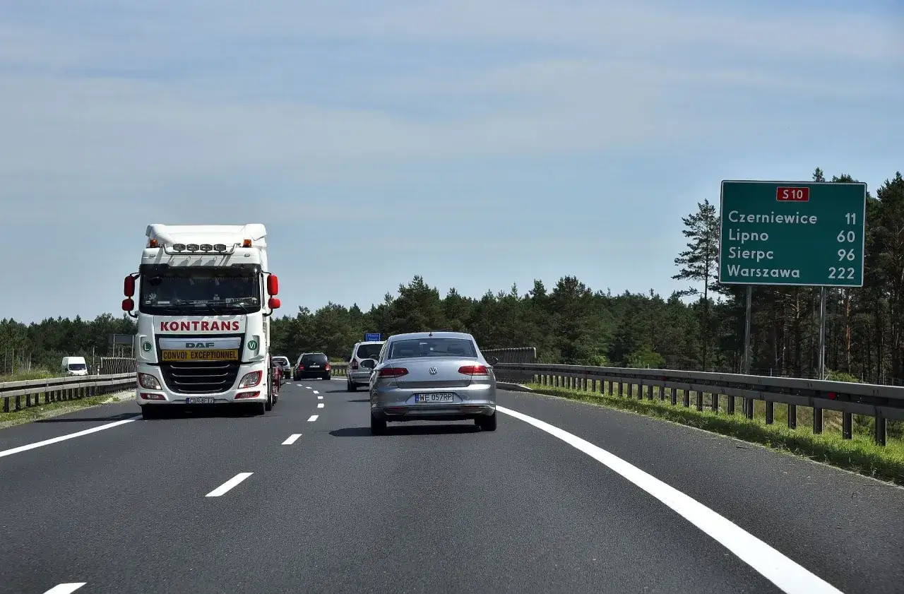 Jadący samochód i ciężarówka na drodze jednojezdniowej dwukierunkowej. Znak S10 wskazuje odległości do Czerniewic, Lipna, Sierpca i Warszawy.