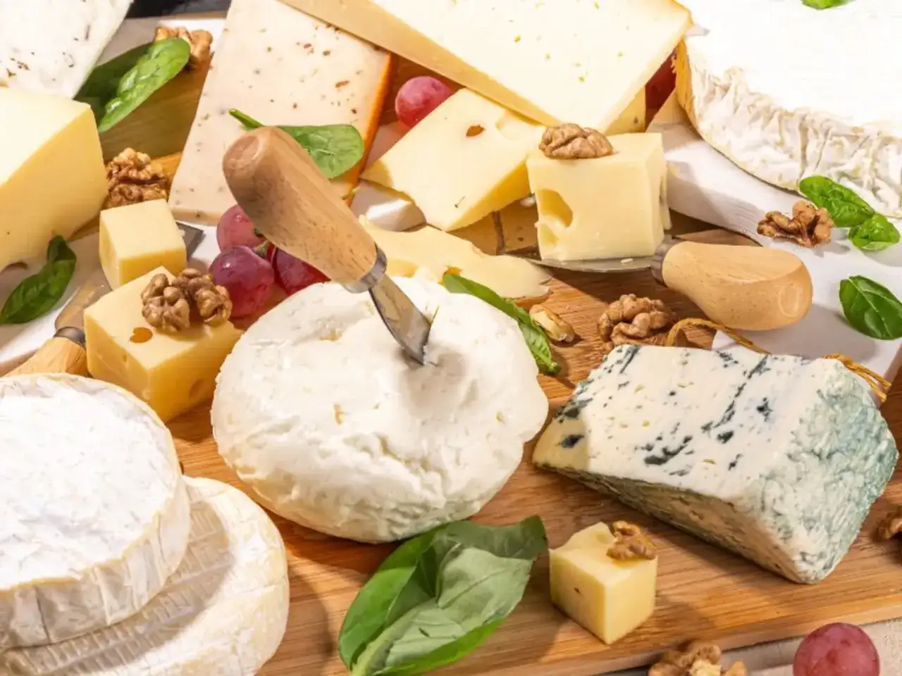 Un assortiment de fromages variés, dont un bleu persillé, un fromage frais et des cubes de fromage, avec des noix et des raisins. Un aperçu du tableau calorique des fromages.