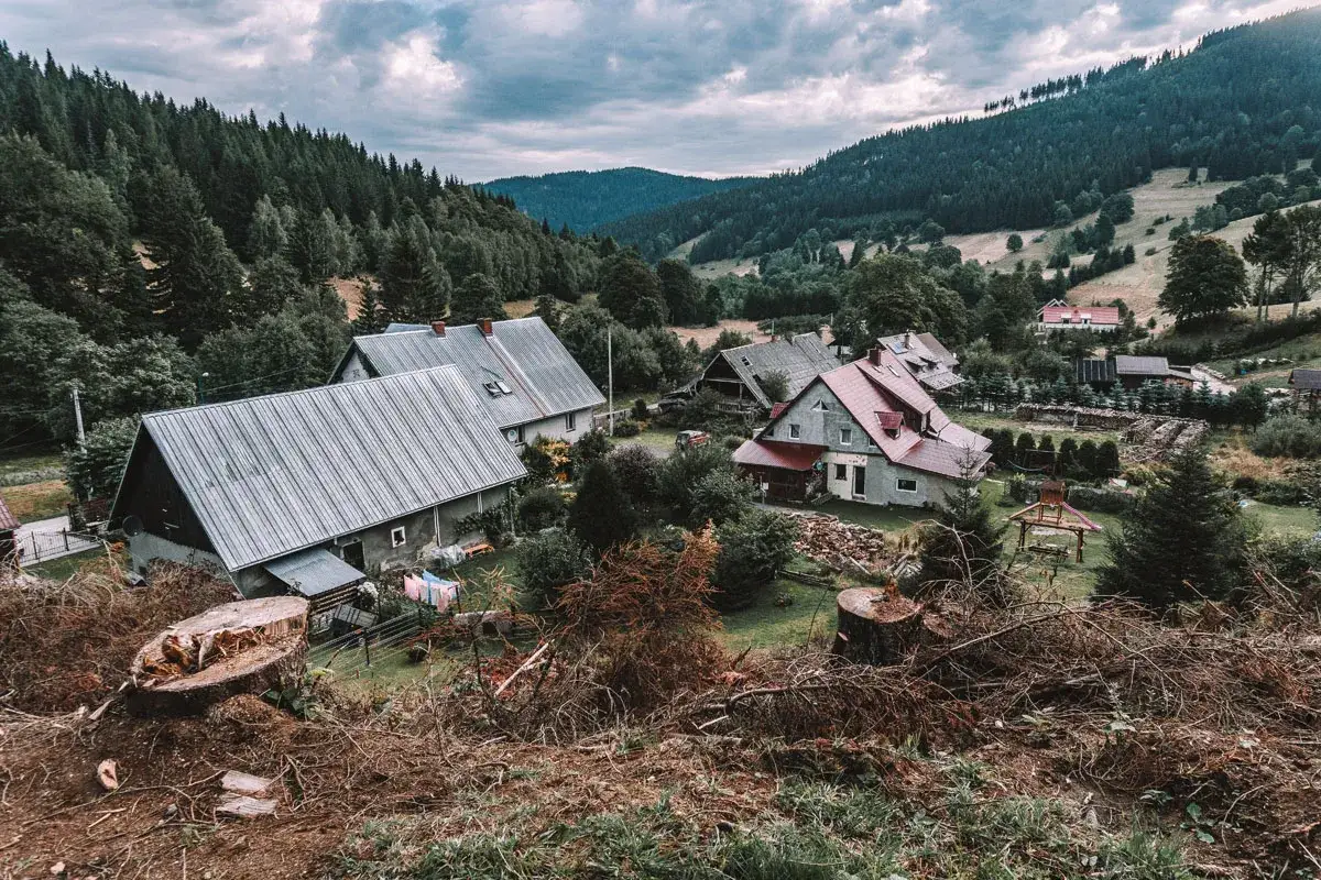 Wioska u podnóża gór, domy z szarymi dachami, lasy i chmury. Widok z góry przypomina kowadło szczyt.