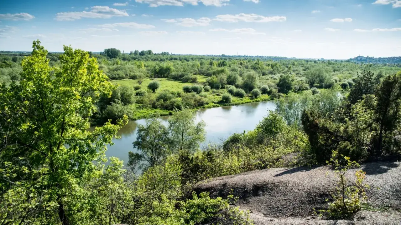 Krajobraz z rzeką i bujną zielenią. W oddali widać miasteczko, jakby wyłaniające się zza **gór pieprzowych**.