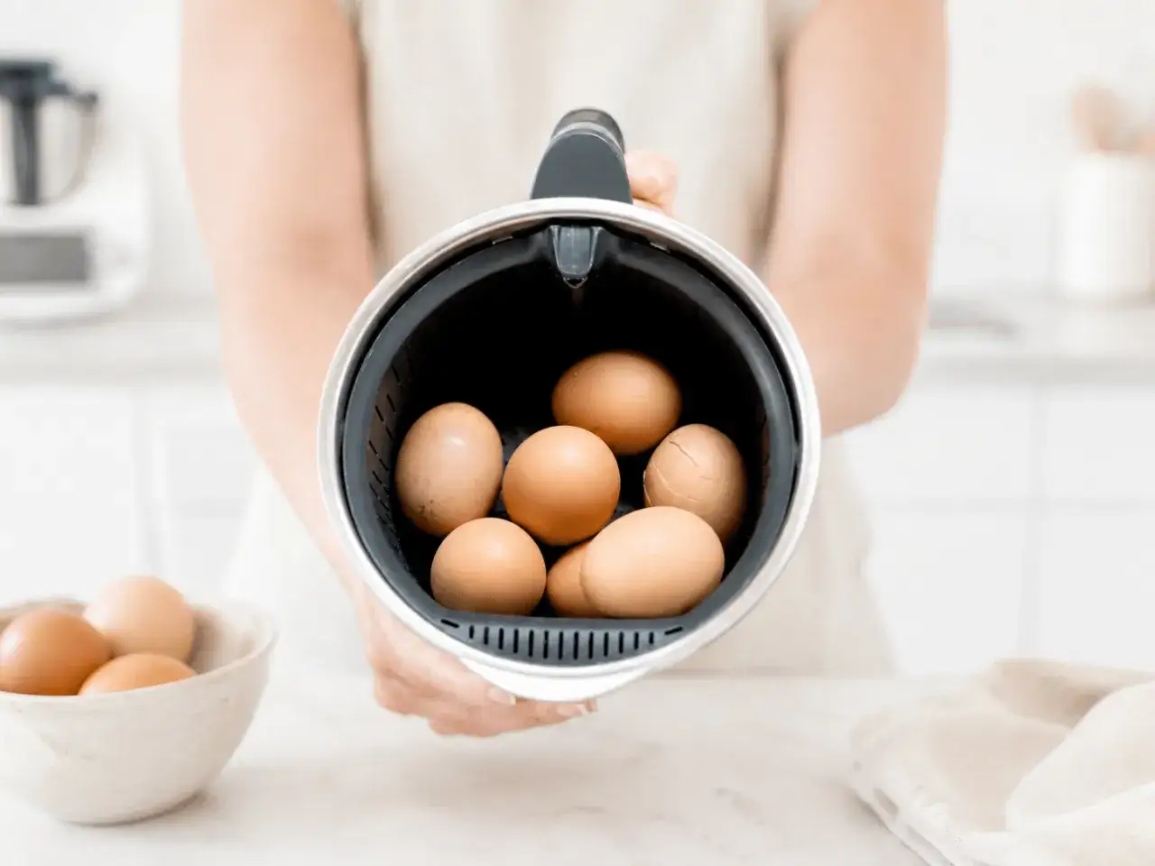 Manos sostienen el recipiente de la Thermomix lleno de huevos para cocer huevos thermomix.