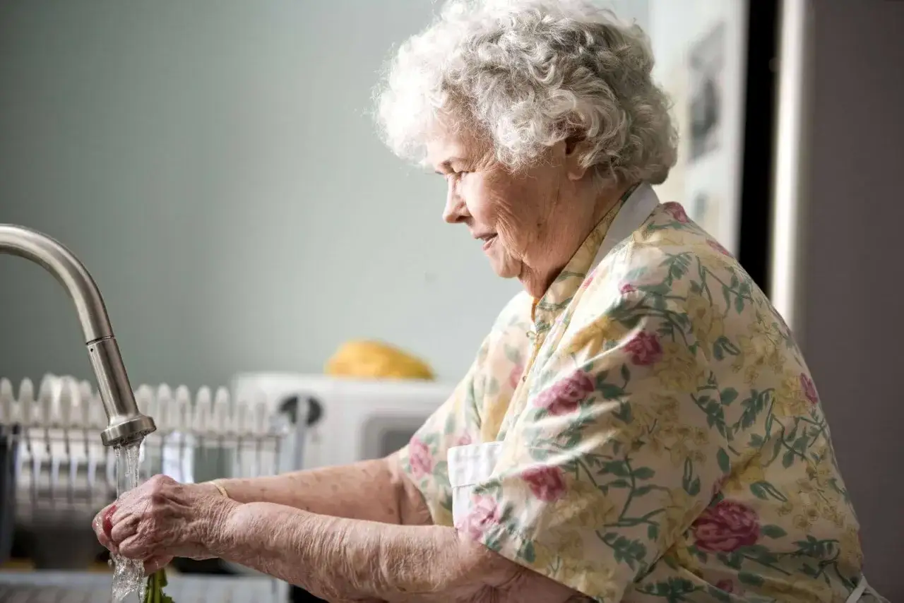 Anziana con Alzheimer lava verdure al lavandino, un gesto semplice per convincerla a prendersi cura di sé.