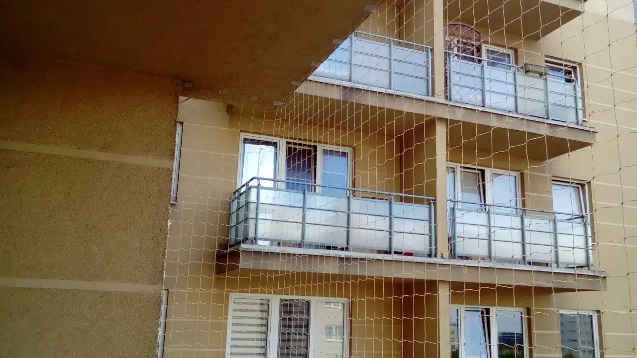 Siatka na balkonie to skuteczne rozwiązanie, jak pozbyć się gołębi. Widać kilka pięter budynku z balkonami zabezpieczonymi siatką.