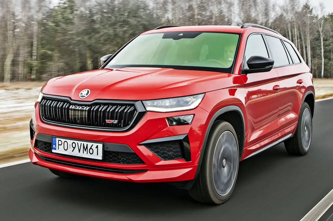 Czerwona Skoda Kodiaq RS pędzi po drodze, otoczona rozmazanym lasem.