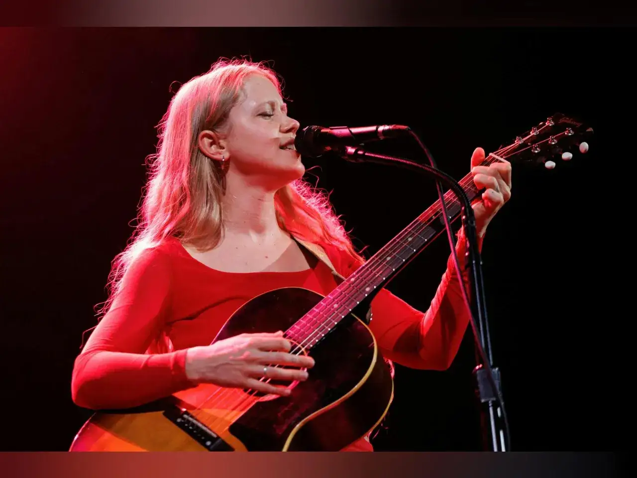 Alice Phoebe Lou singt und spielt Gitarre auf der B&uuml;hne in Berlin, ihr rotes Oberteil leuchtet im Scheinwerferlicht.