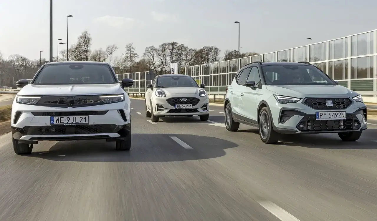 Trzy małe crossovery jadące obok siebie po drodze. Biały Opel Mokka, jasnoszary Ford Puma i jasnoszary Seat Arona.