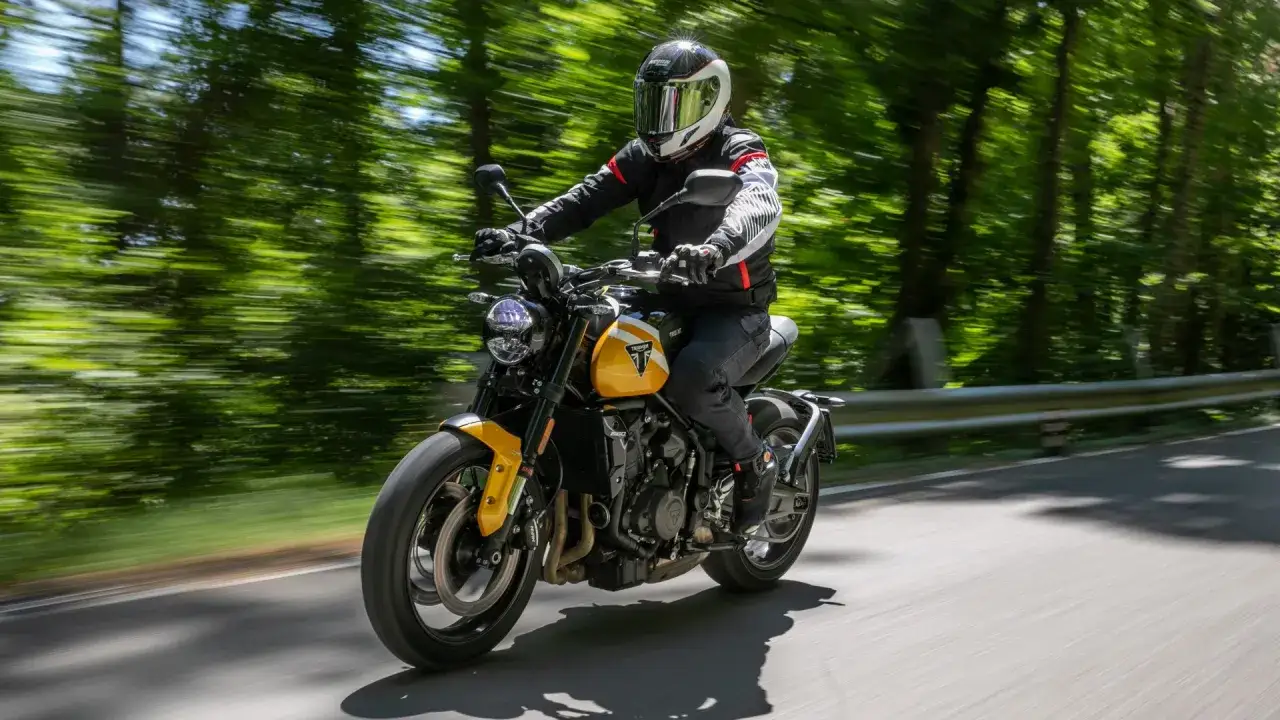 Motociclista su una moto gialla sfreccia su una strada alberata. L'altezza sella moto permette una guida comoda e sicura.