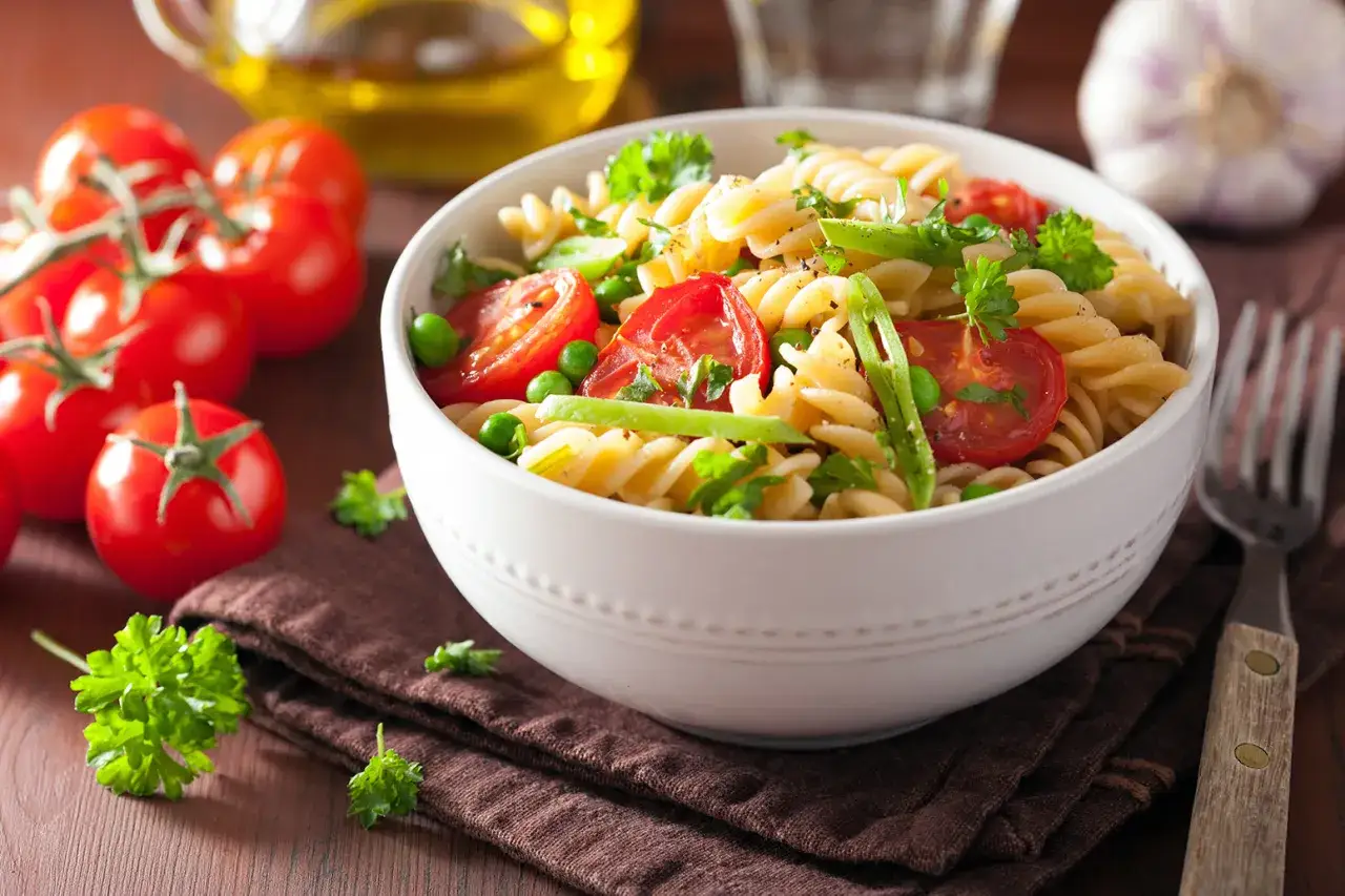 Un plato de pasta con verduras frescas, como tomates cherry, guisantes y perejil, servido en un cuenco blanco.