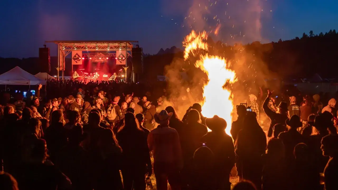 Foule en délire devant un groupe de metal année 90, un immense feu de joie illumine la scène.