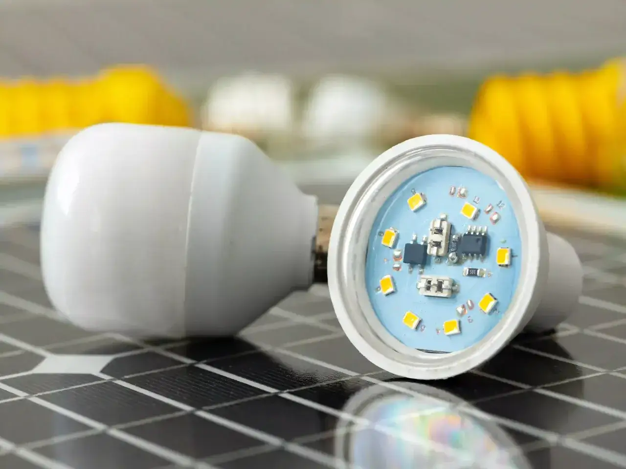 Comment reconna&icirc;tre une ampoule LED : une ampoule blanche ouverte r&eacute;v&egrave;le ses puces lumineuses sur un fond bleu, pos&eacute;e sur un panneau solaire.
