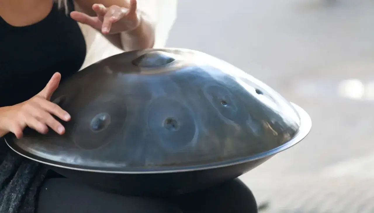 Ręce delikatnie uderzają w metalowy instrument, tworząc melodyjne dźwięki. Dowiedz się, jak grać na drumli.